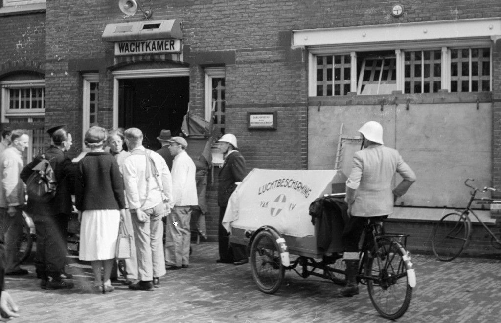Foto Hans Sibbelee, Collectie Nederlands Fotomuseum. Een gewonde van het zgn. "Dam-incident', waarbij enkele leden van de Kriegsmarine ineens het vuur openden op de feestende menigte op de Dam te Amsterdam, wordt met een tot ambulance omgebouwde bakfiets van de Dienst Luchtbescherming naar het Binnengasthuis gebracht (7 mei 1945)